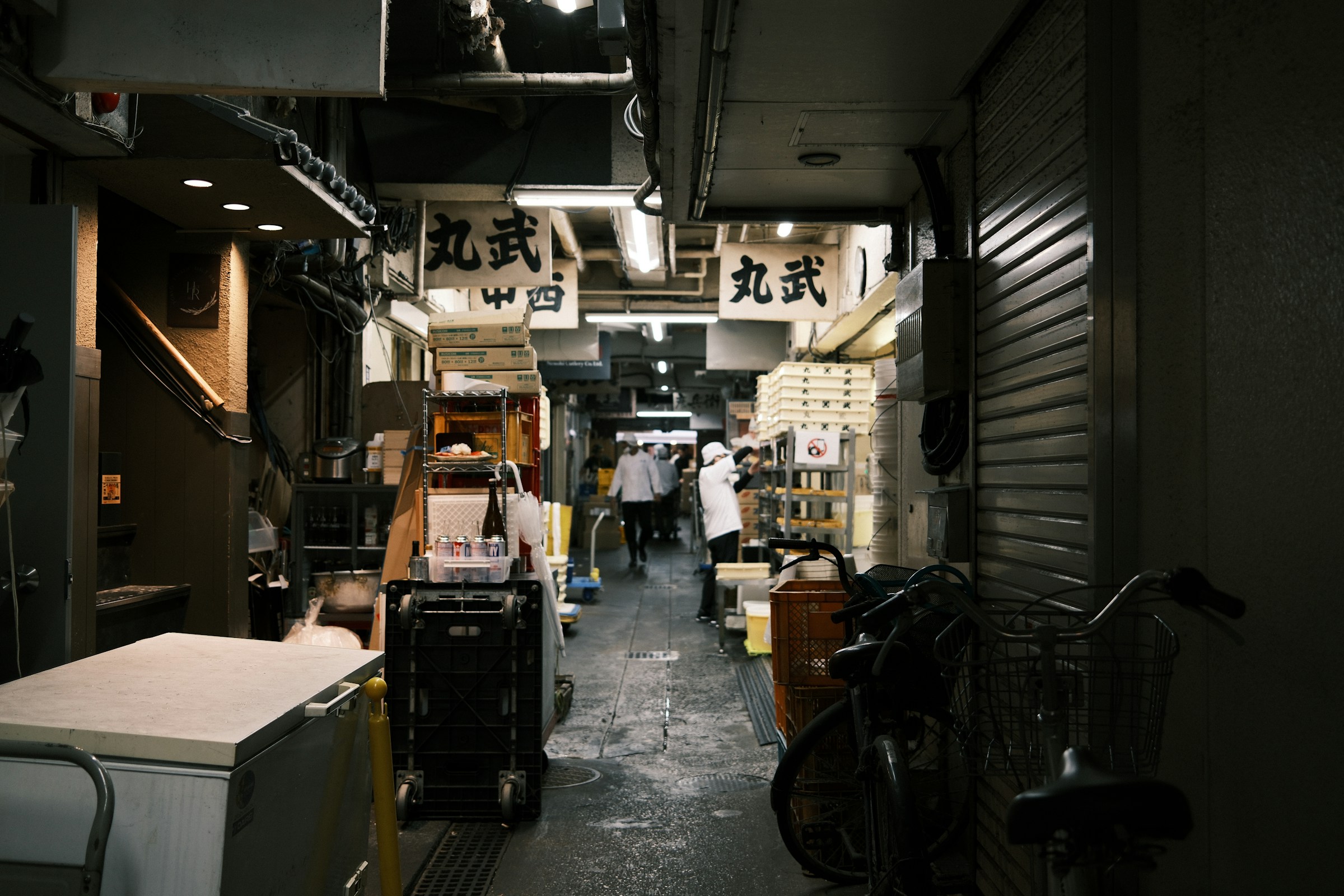 Corredor de trabalho no mercado de Tsukiji, com caixas, utensílios e profissionais.